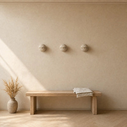 Trois appliques murales en pierre alignées au-dessus d'un banc de chêne dans une entrée, lumière naturelle | Delvanie