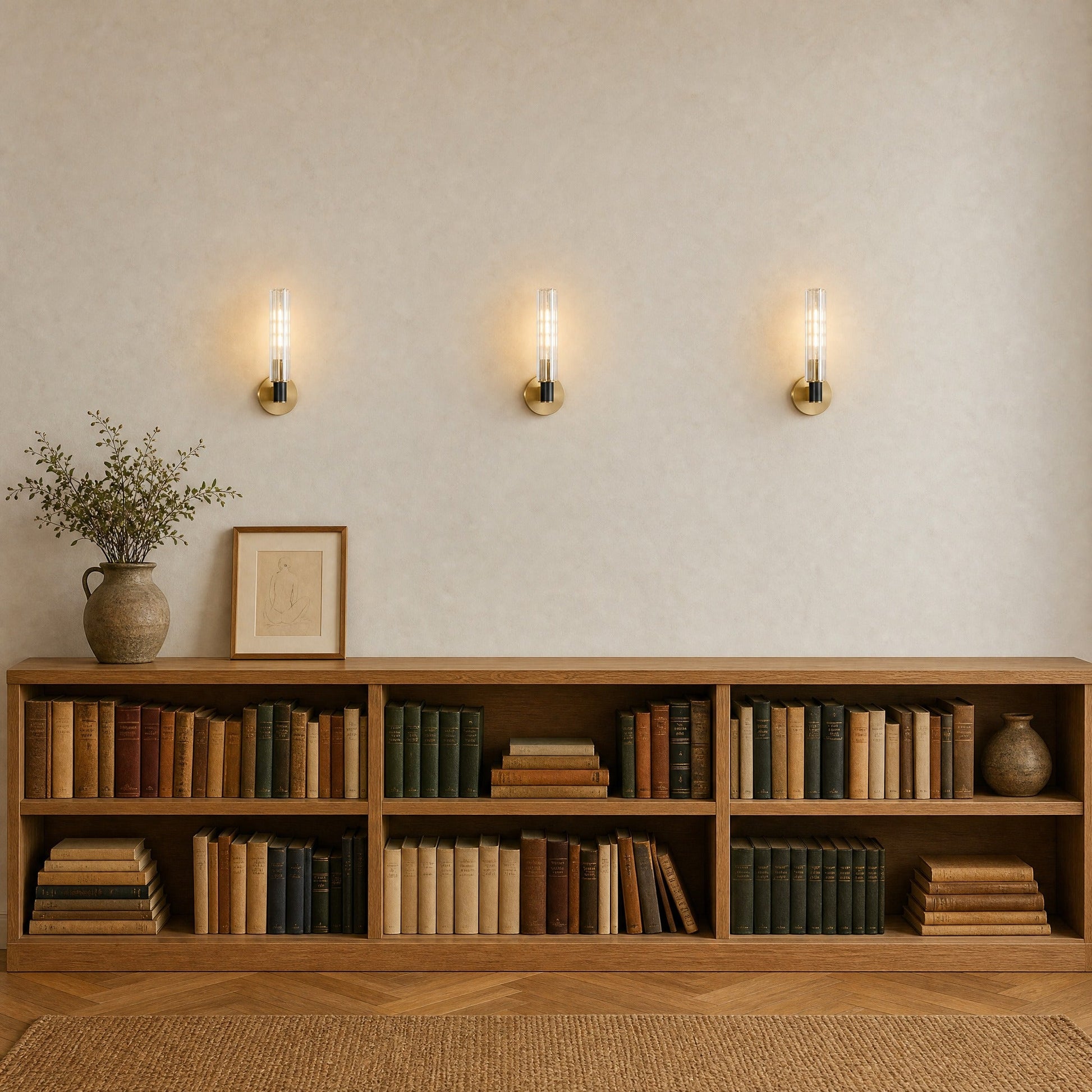 Trois appliques murales cristal alignées et allumées au-dessus d'un rayonnage de chêne, couloir bibliothèque | Delvanie