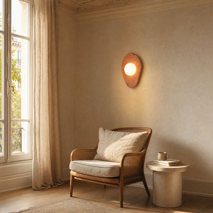 Applique murale terracotta format Galet allumée au-dessus d'un fauteuil en cannage dans un coin lecture | Delvanie
